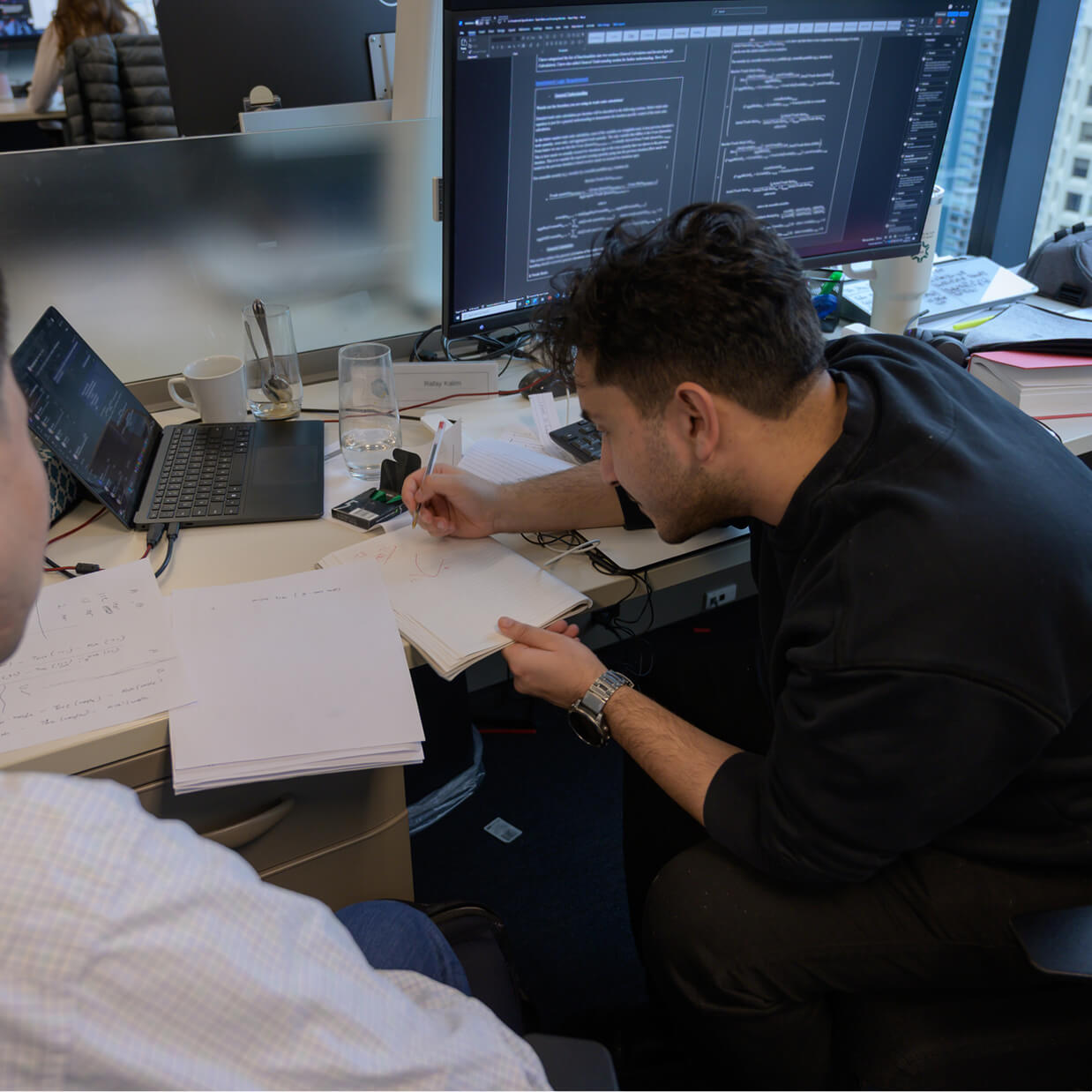 A Q Team member writing on a piece of paper while sitting at their desk.